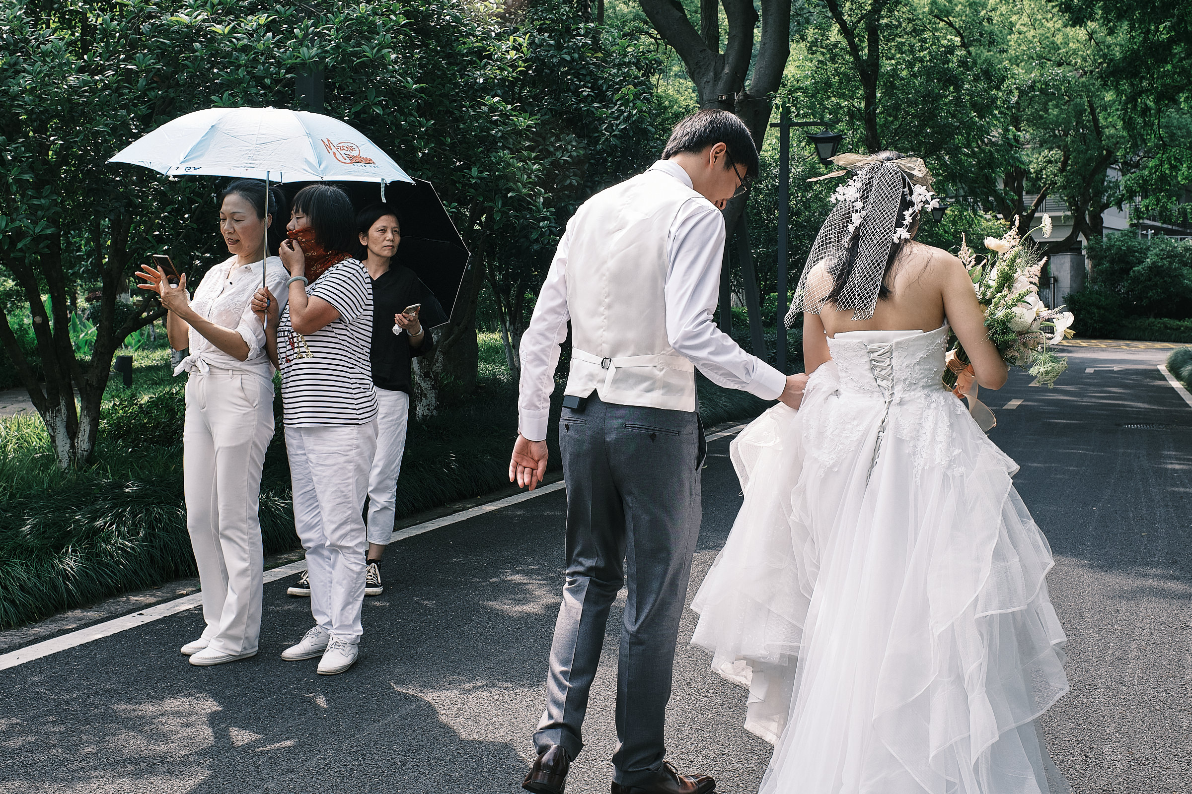 groom holds the bride and her dress as they walk and strangers look at them in the park