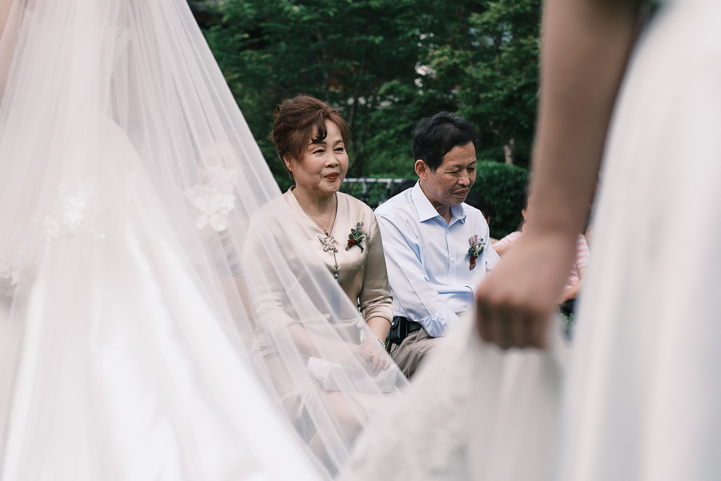 father and mother of groom framed by the hand of the bridesmaid holding the dress of the bride in hangzhou china