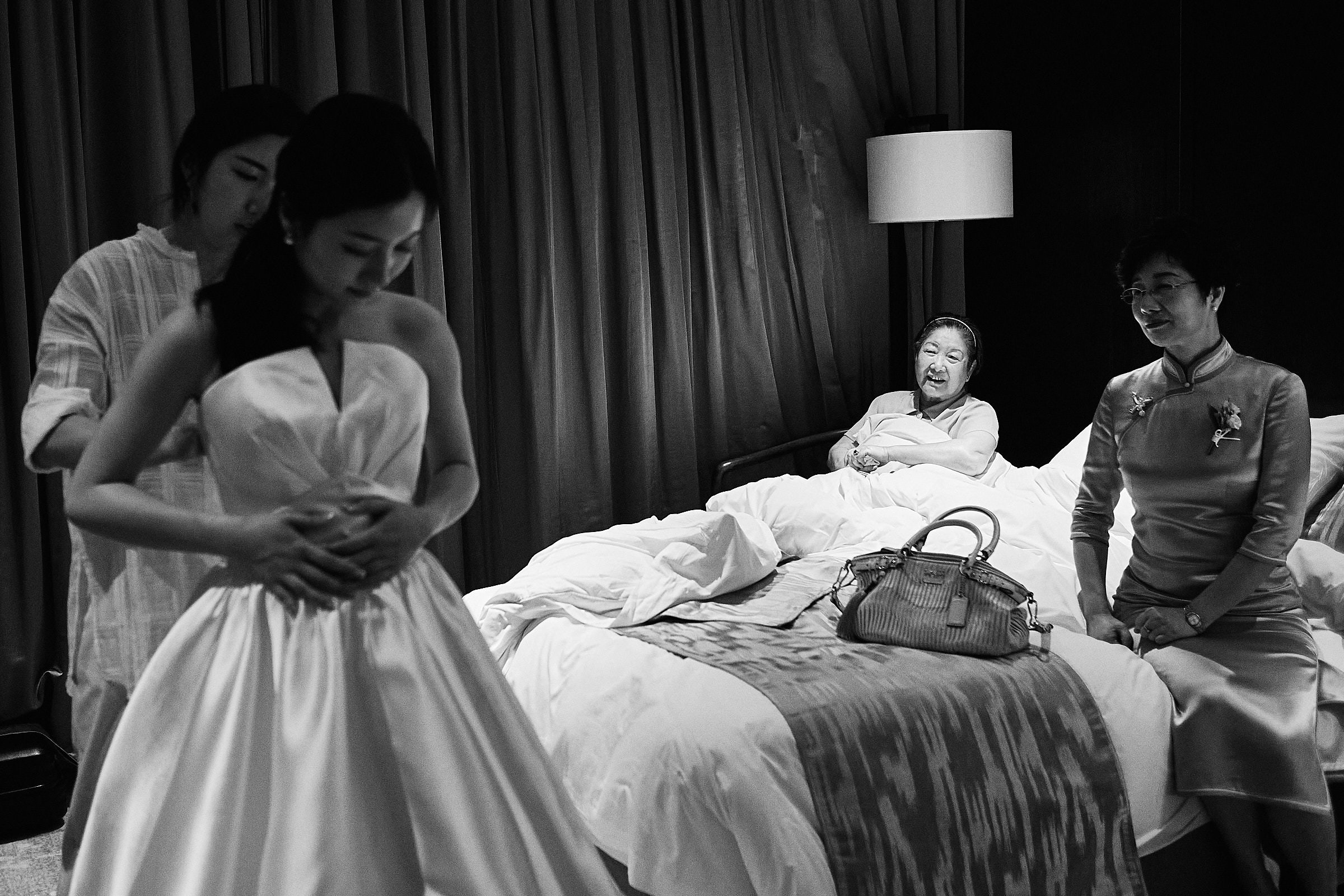 Black And White Image Of Bride Putting On Her Dress As Her Grandmother And Mother Look At Her In China