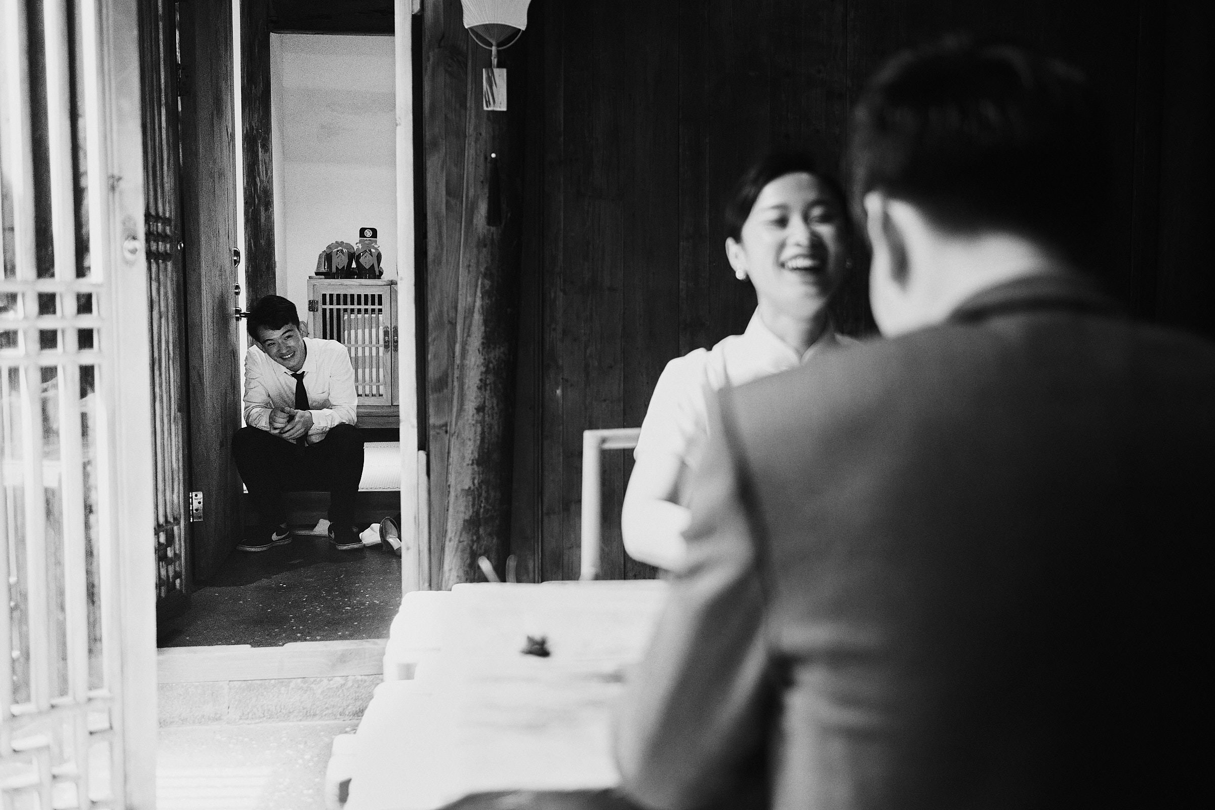 Bride And Groom Laugh As Brother Of The Bride Sits In Door Frame And Laughs Too