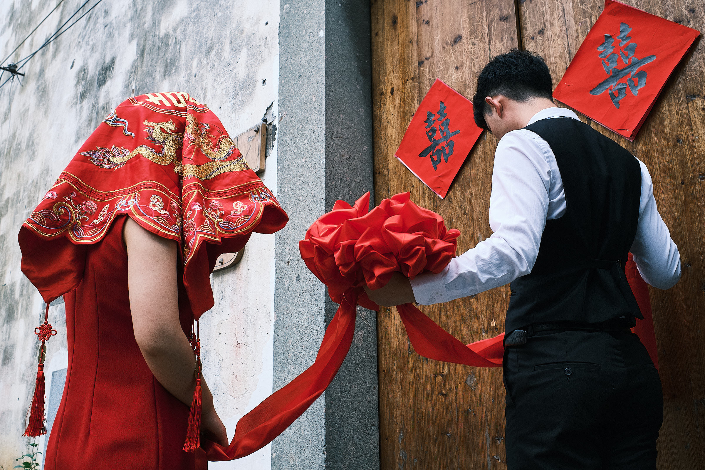 The Bride Dressed In Red And Her Brotber Stand Next To The Entrance Of Wedding Ceremony In China