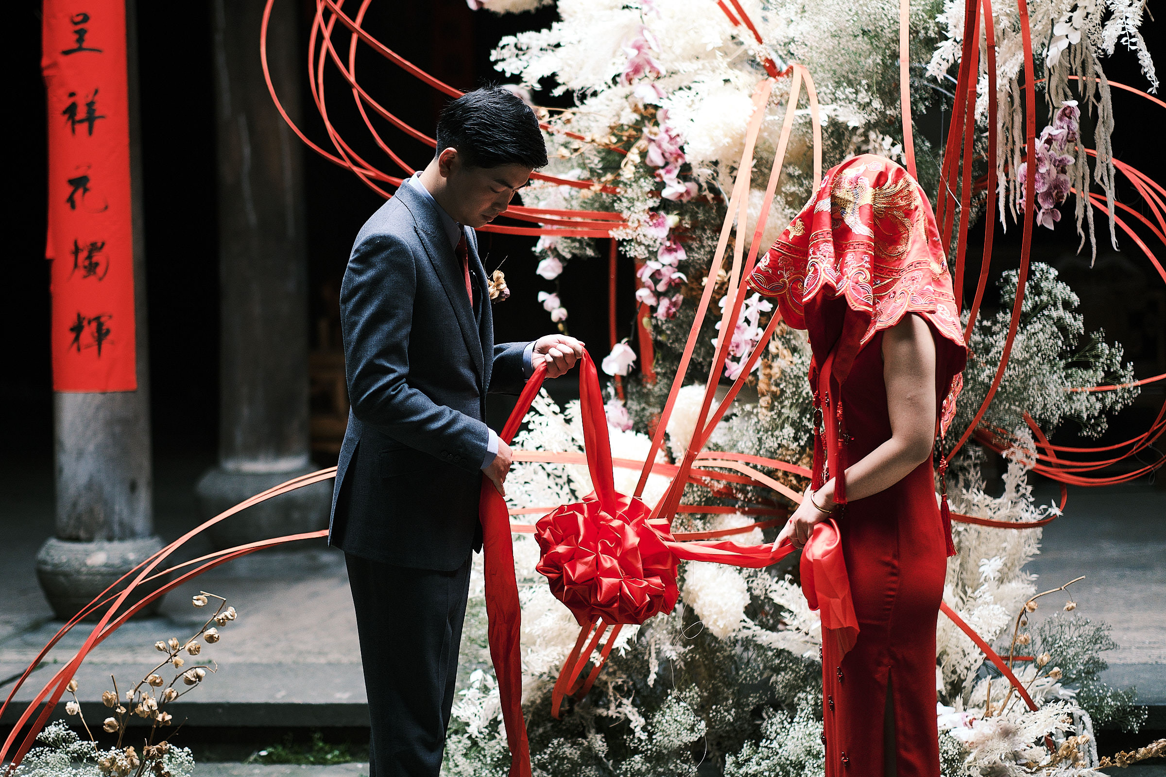 Groom And Bride With Covered Red And Dressed In Red Stand In Front Of Floral Sculpture Decorations