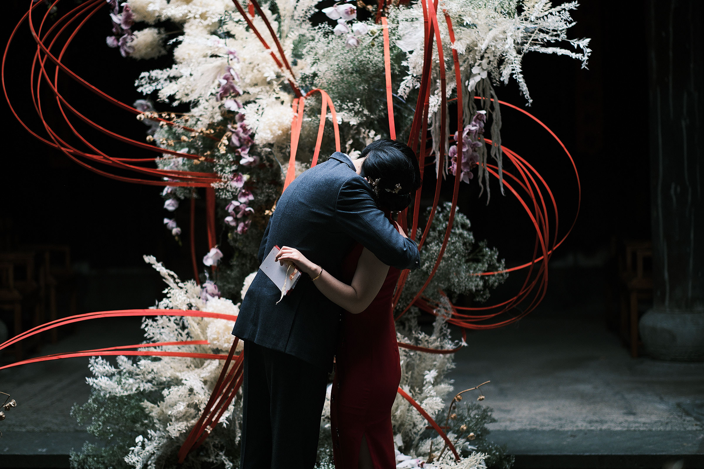 Groom Hugs Bride At China Wedding Ceremony In Front Of Floral Scultpture Arrangement