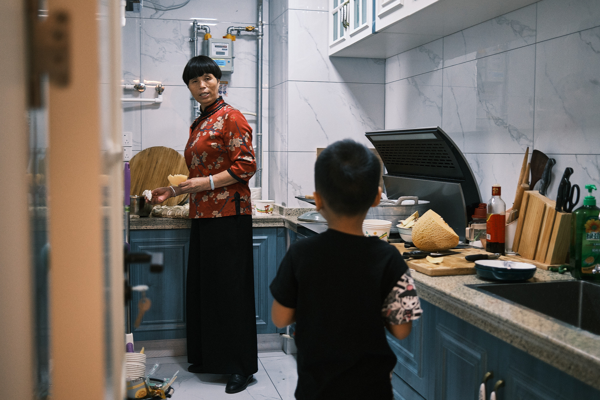 Boy In Kitchen Looks At Aunt As She Finishes Preparing Dumplings