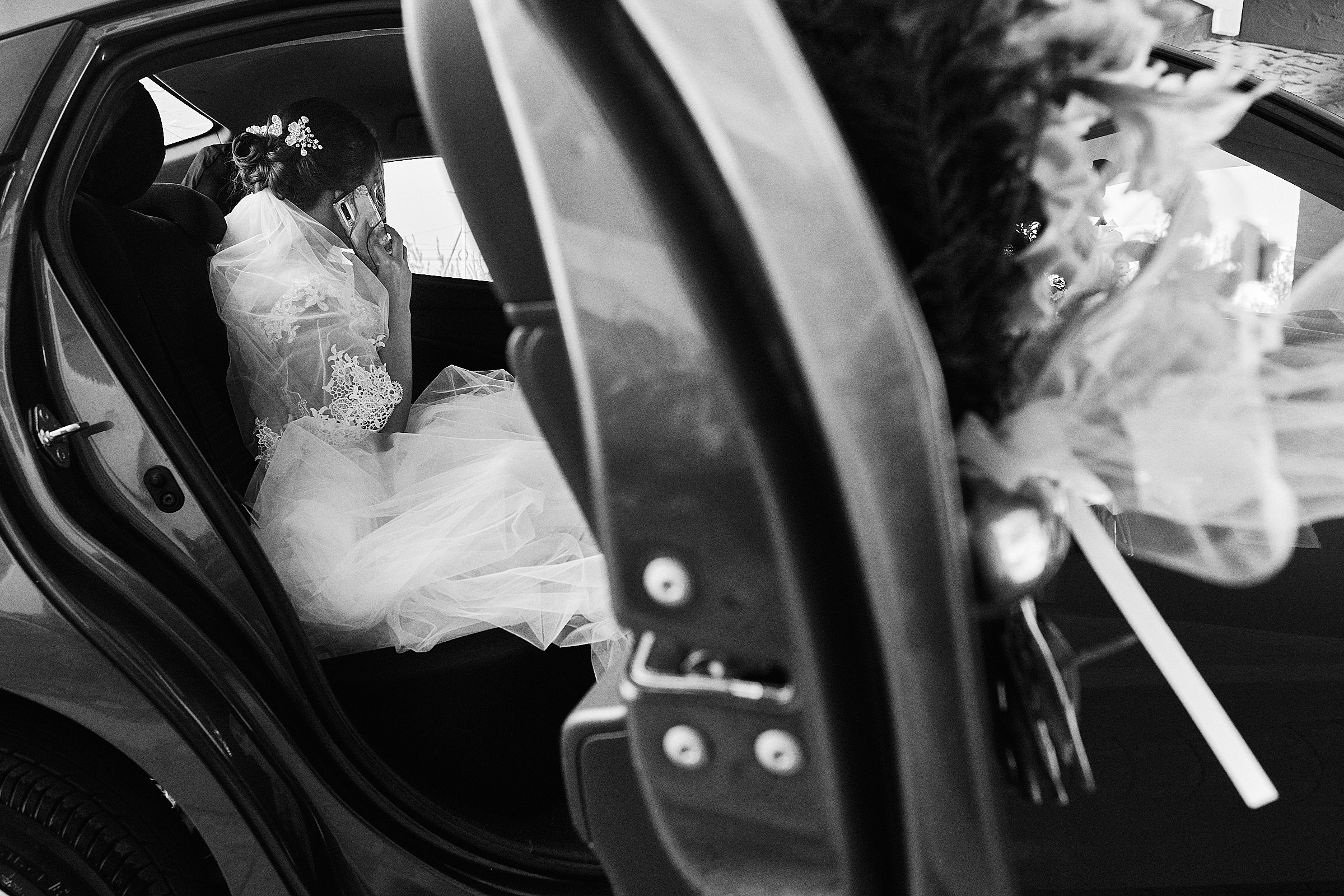 Black And White Image Of Bride On Phone Inside Car