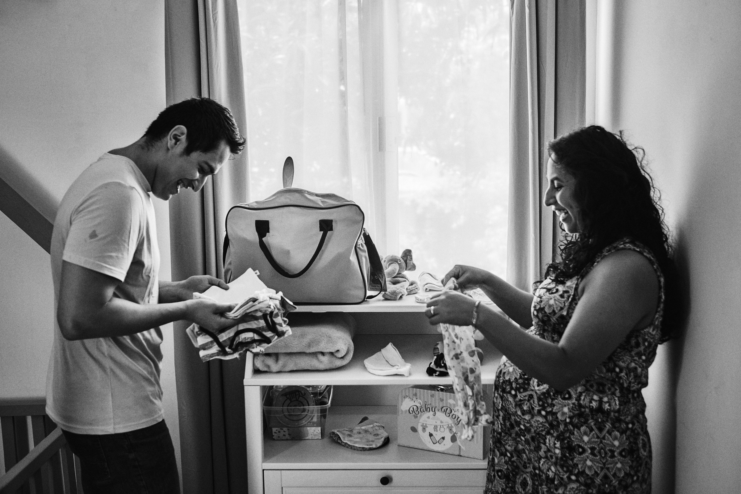 Husband And Wife Fold The Clothes Of Their Newborn In Black And White