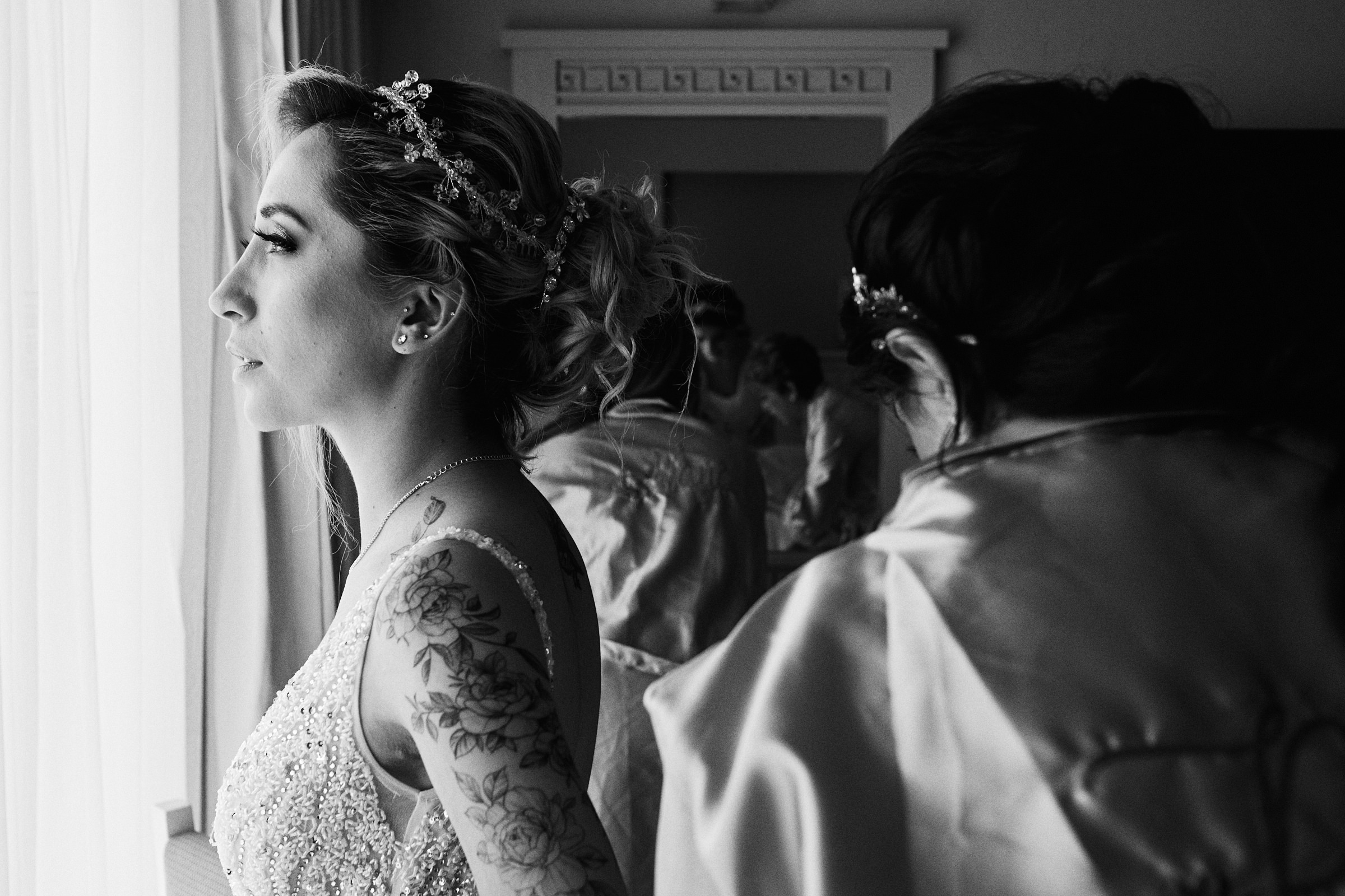 Black And White Image Of Bride Looking At The Window As She Gets Dressed For Her Wedding In Mexico