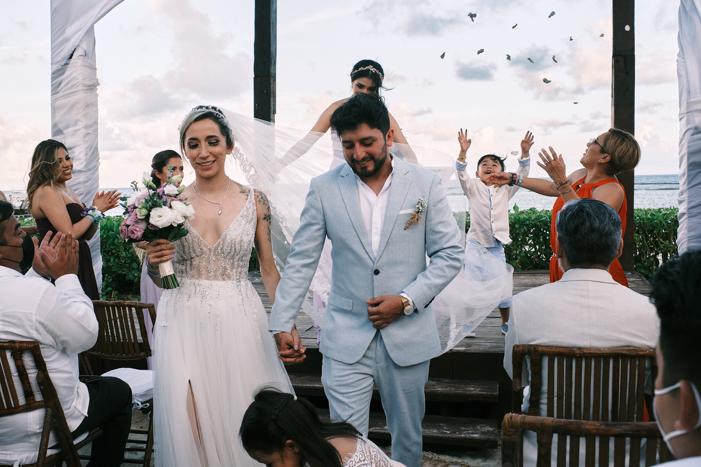 Bride And Groom Exit Their Ceremony As Their Son Throws Petals In The Air